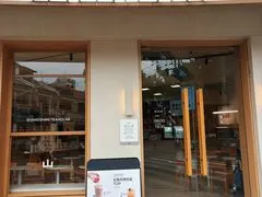 Nhìn qua cửa kính vào không gian gỗ sáng màu bên trong quán, có bàn ghế và biển hiệu nhỏ đặt trước cửa